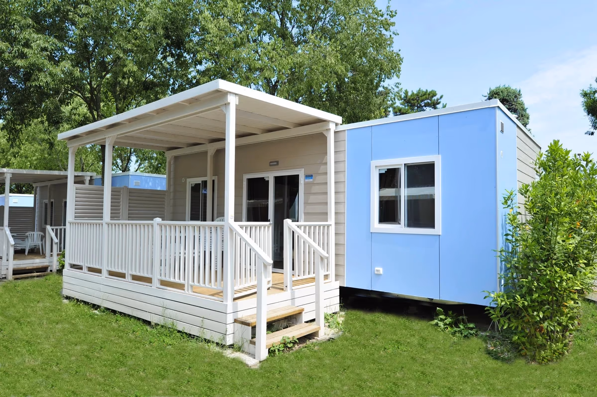 Stacaravan met een wit overdekt terras en een lichtblauwe zijgevel op Camping Bella Italia, met gras eromheen