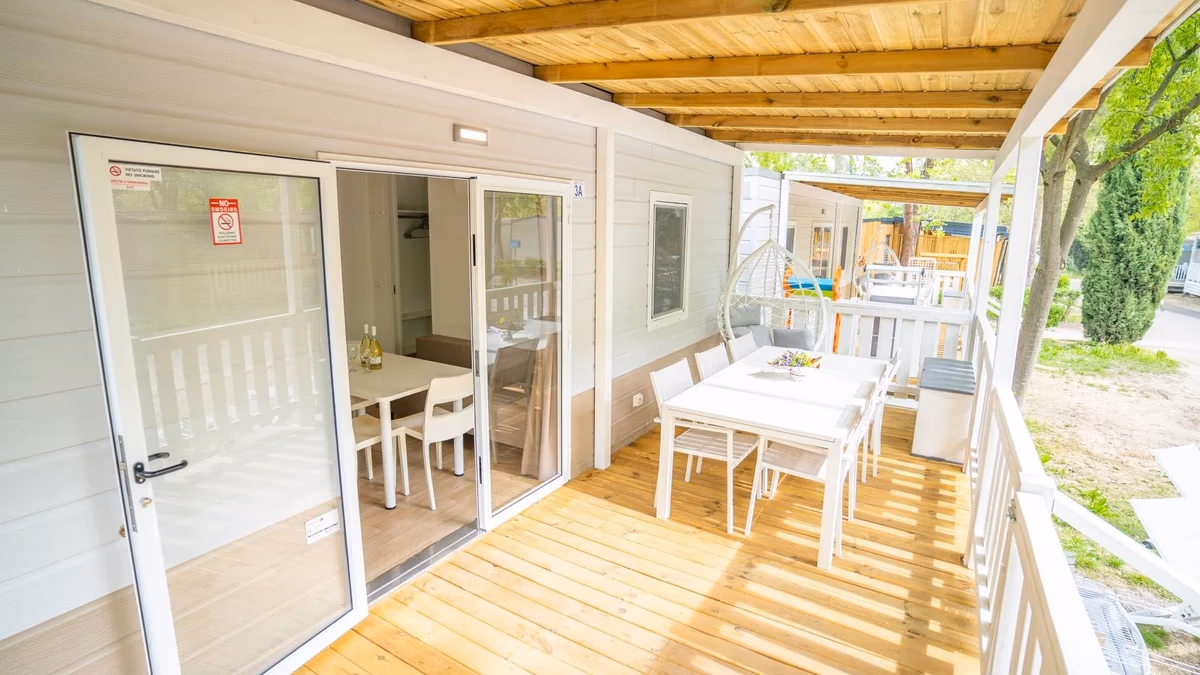 Licht overdekt terras met een witte eettafel en een hangstoel bij een stacaravan op Camping Bella Italia, met schuifpui naar binnen