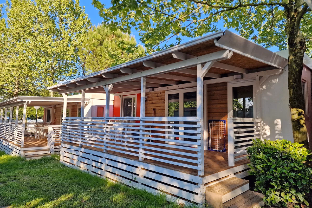 Stacaravan met een houten gevel en een wit overdekt terras op Camping Bella Italia, met een hondenbench op de veranda