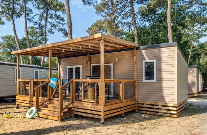 Stacaravan met een houten overkapping boven een ruim terras op Camping Bella Italia, tussen de parasoldennen, met een zwemband in het zand