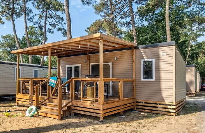 Stacaravan met een houten overkapping boven een ruim terras op Camping Bella Italia, tussen de parasoldennen, met een zwemband in het zand