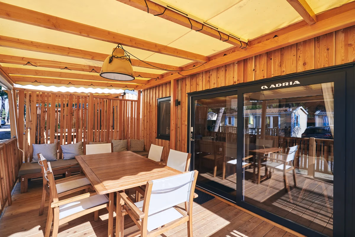 Houten terras onder een gele luifel met een teakhouten eettafel en loungebank bij een stacaravan op Camping Bella Italia