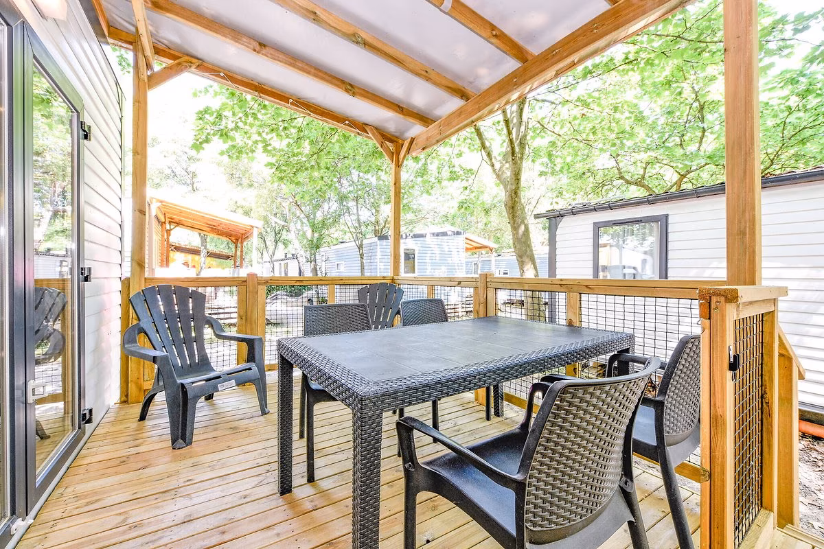 Houten terras onder een lichte overkapping met een rieten eettafel en stoelen bij een stacaravan op Camping Bella Italia