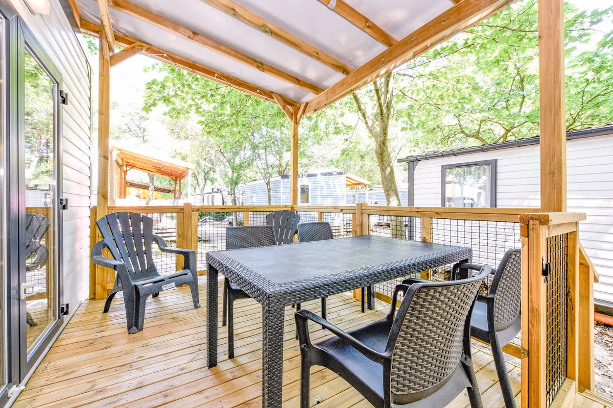 Houten terras onder een lichte overkapping met een rieten eettafel en stoelen bij een stacaravan op Camping Bella Italia