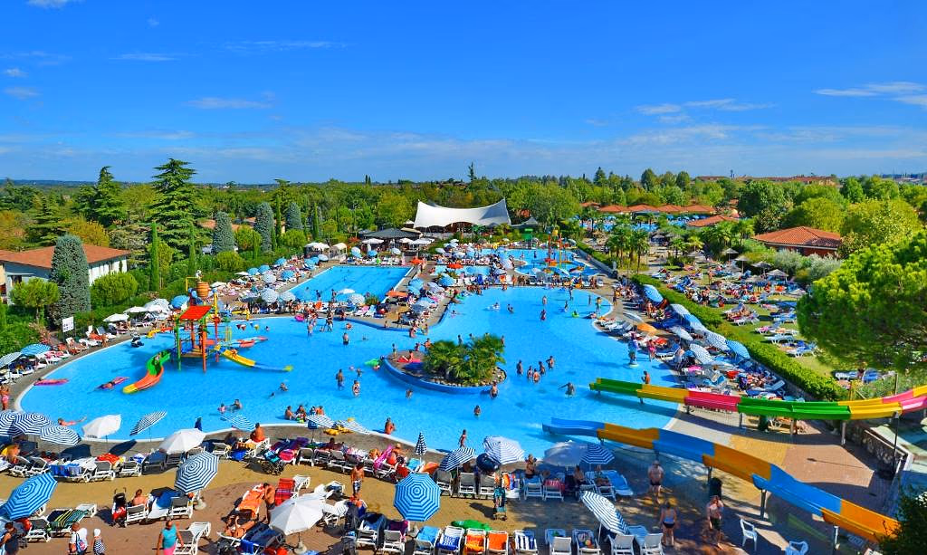 Aquapark van Camping Bella Italia met een groot lagunebad, gekleurde glijbanen en rijen ligbedden onder parasols