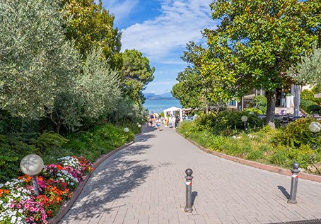 Bloemenrijke laan tussen bomen en accommodaties op Camping Bella Italia bij Peschiera del Garda
