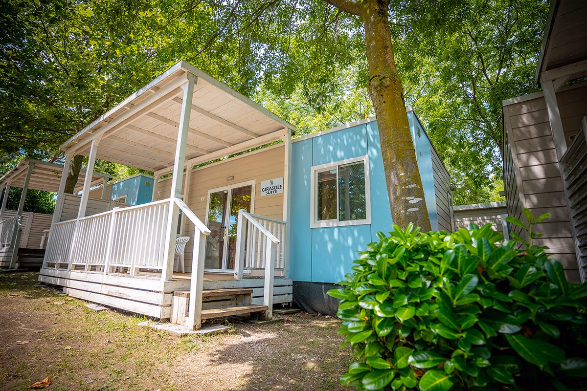 Buitenkant van de Girasole Suite stacaravan met veranda tussen de bomen op Camping Bella Italia