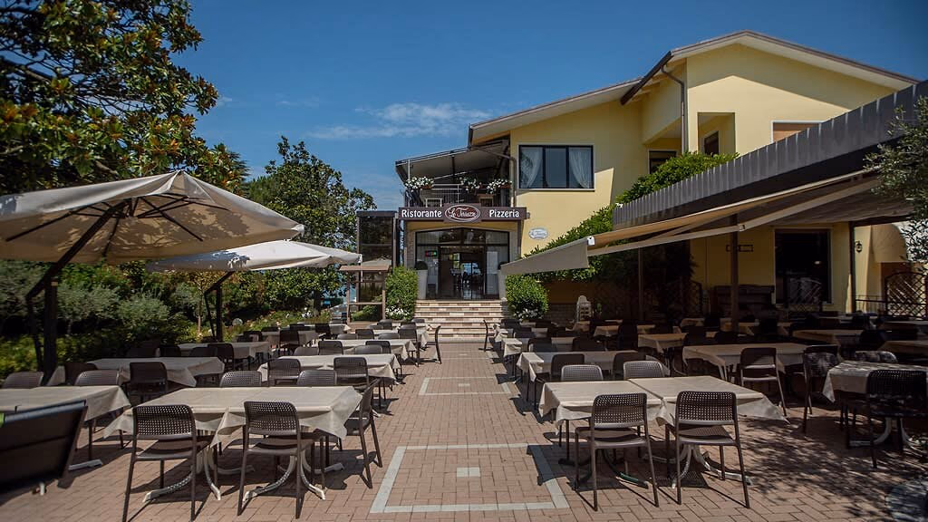 Buitenterras met tafels en parasols bij een restaurant op Camping Bella Italia
