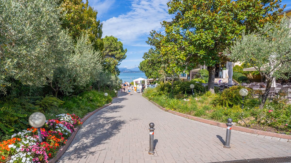 Groene laan met bloemen en hoge bomen op Camping Bella Italia in Peschiera del Garda