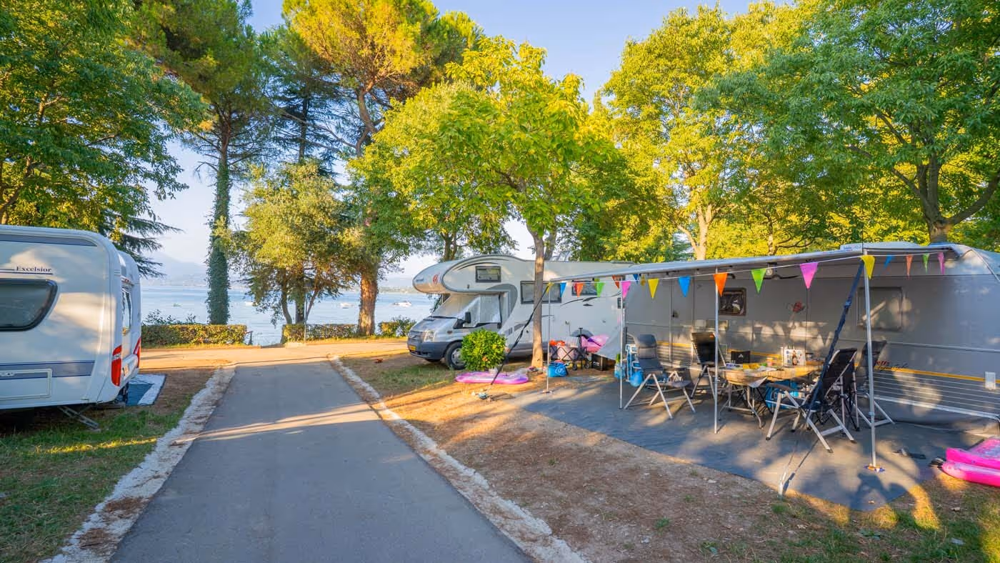 Kampeerplaats met voortent onder hoge bomen op Camping Bella Italia