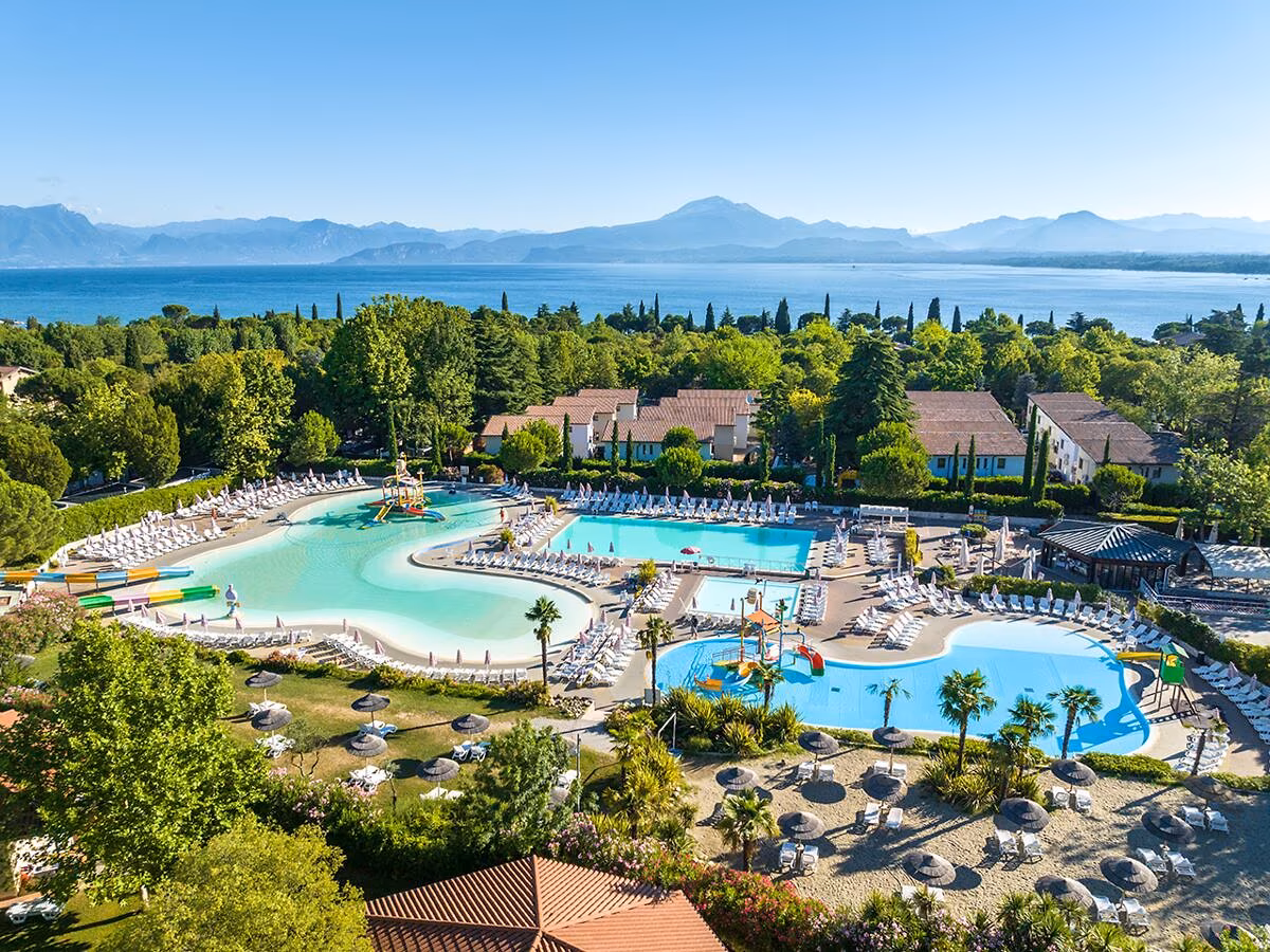Luchtfoto van de zwembaden van Camping Bella Italia met daarachter de vakantiehuizen en het Gardameer