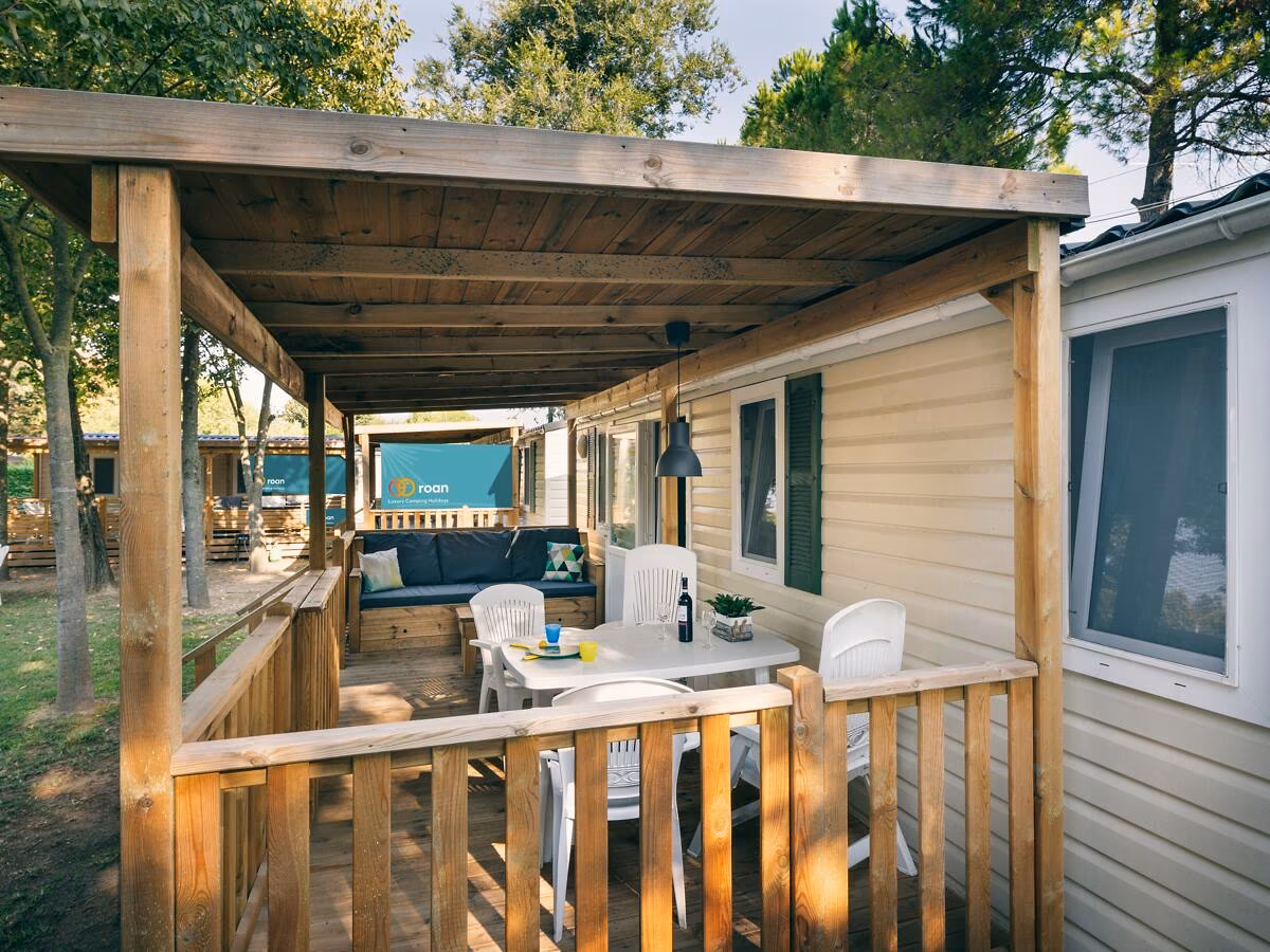 Veranda met een witte eettafel en stoelen onder een houten balkenkap bij een stacaravan op Camping Bella Italia