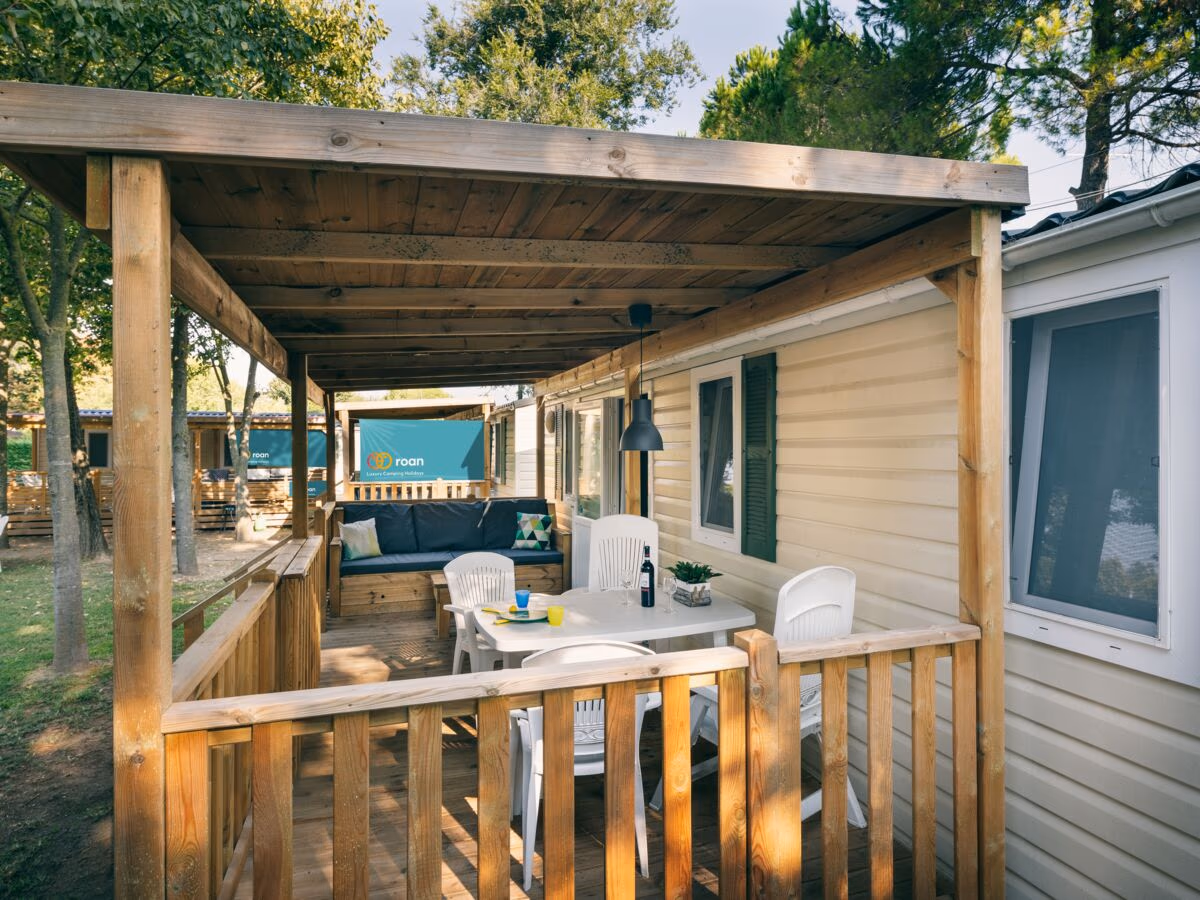 Veranda met een witte eettafel en stoelen onder een houten balkenkap bij een stacaravan op Camping Bella Italia