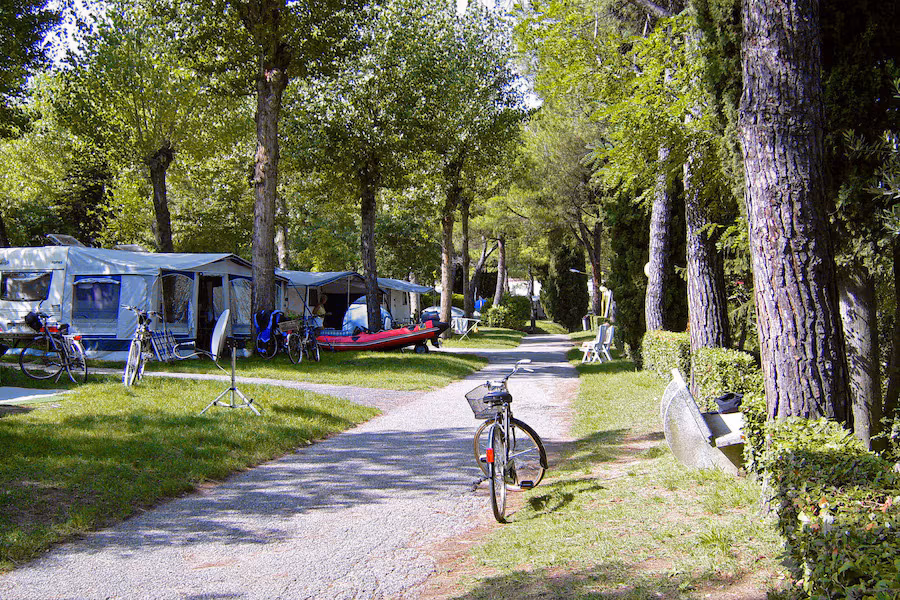 Ruime kampeerplaatsen tussen hoge bomen op Camping Bella Italia aan het Gardameer