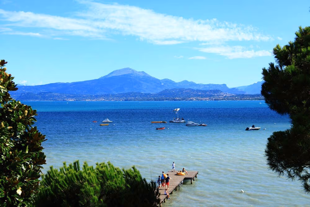 Kiezelstrand met helder water en bergen aan het Gardameer bij Camping Bella Italia