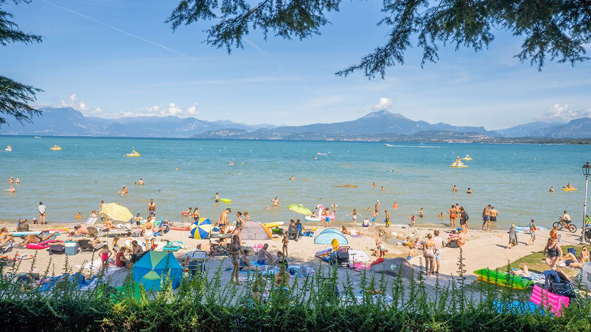 Strand van Camping Bella Italia met zwemmers en uitzicht op de bergen rond het Gardameer