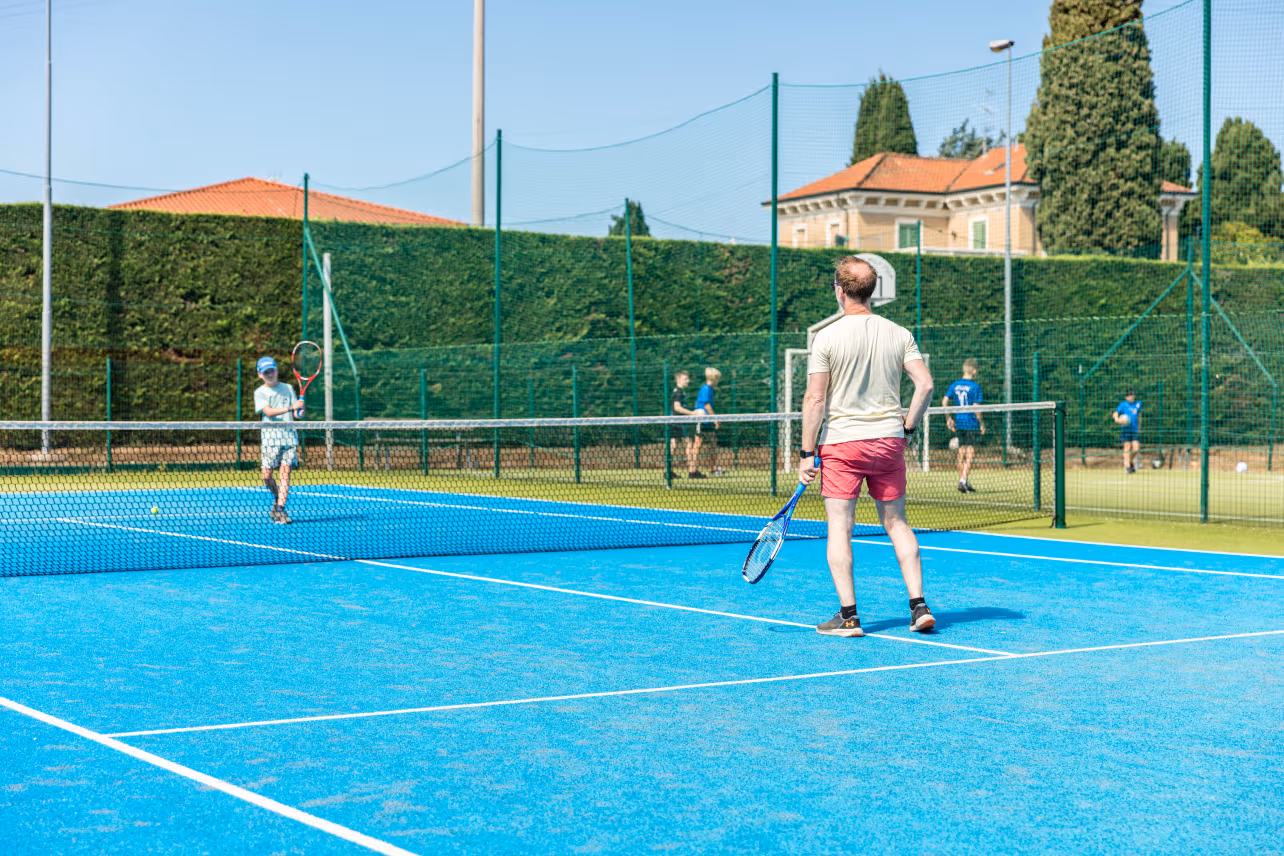 Gasten spelen tennis op de blauwe tennisbaan van Camping Bella Italia in Peschiera del Garda