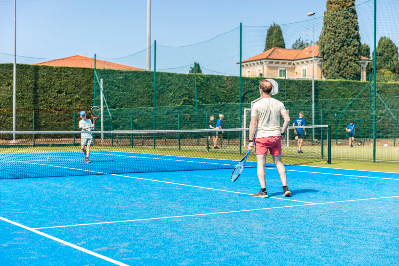 Gasten spelen tennis op de blauwe tennisbaan van Camping Bella Italia