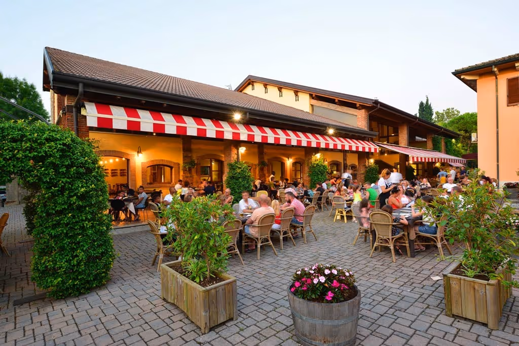 Gezellig buitenterras van Trattoria Bella Italia met gasten aan tafel op de camping