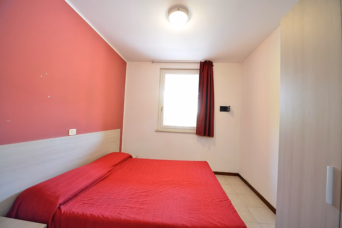 Tweepersoonsslaapkamer met rood bed in appartement Ibisco op Camping Bella Italia
