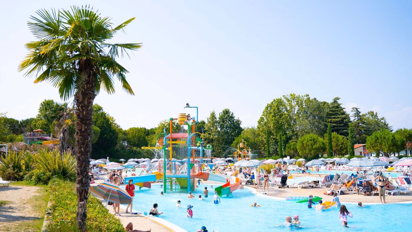 Breed overzicht van het aquapark met palmbomen en waterspeeltoestellen op Camping Bella Italia