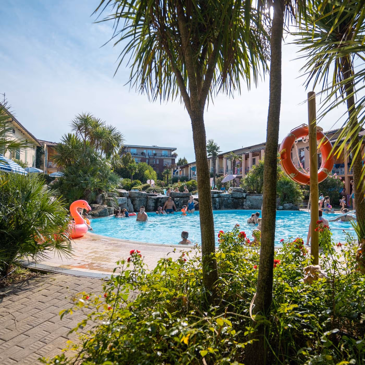 Zwembad van Camping Bella Italia gezien tussen palmbomen en beplanting