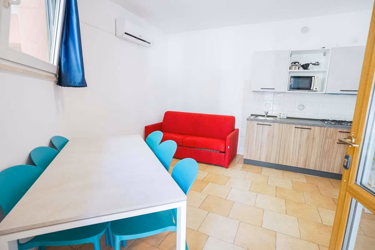 Woonkeuken met eethoek en gekleurde stoelen in een Oleandro-bungalow van Camping Bella Italia