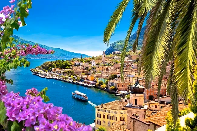 De haven van Limone sul Garda met bloeiende bougainvillea op de voorgrond en een boot op het blauwe meer